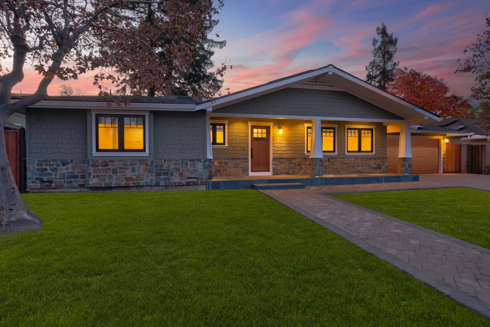 Exterior of a Bay Area Craftsman home at dusk after a full renovation, with a stone porch, new siding and new landscaping.