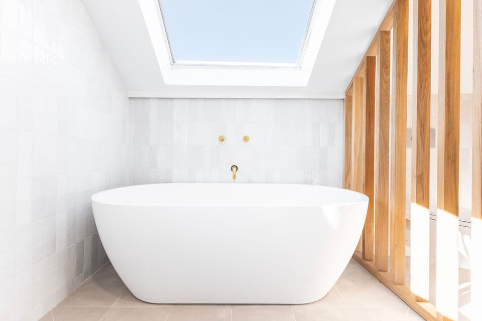 Freestanding soaking tub under a skylight with white tile and a wood slat partition