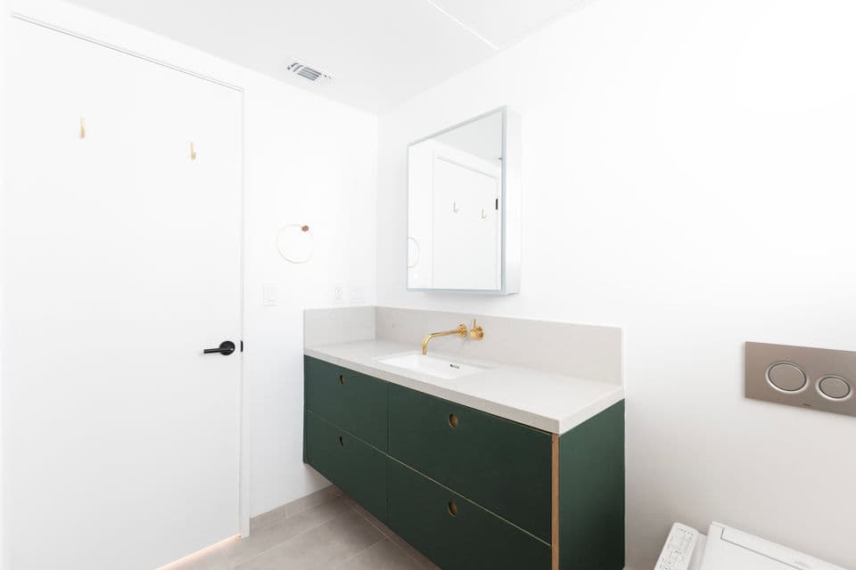 Modern bathroom with floating green vanity, brass wall-mounted faucet, and quartz counter