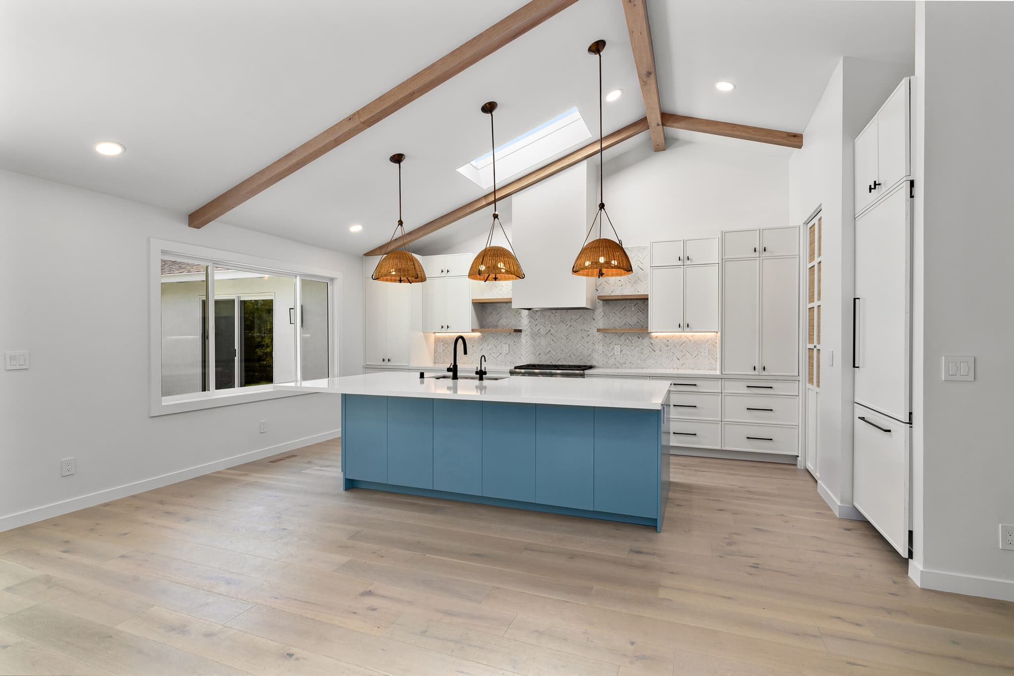 Open kitchen with vaulted wood-beam ceiling, skylight, blue island, and rattan pendant lights