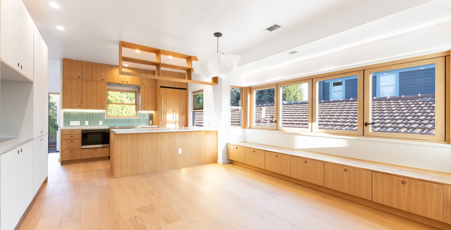 White oak kitchen with window bench seating, green tile backsplash, and built-in storage wall