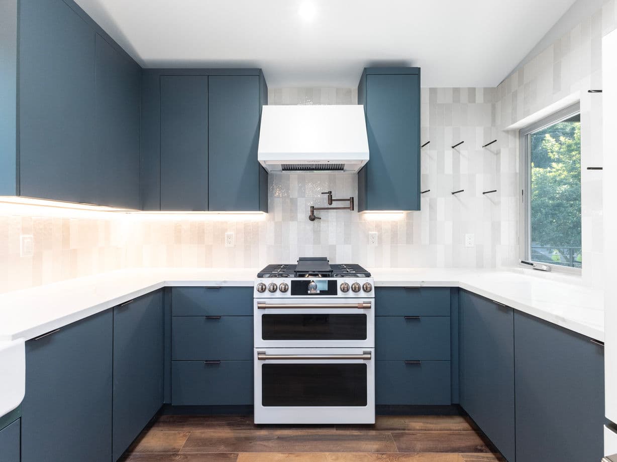 Deep blue kitchen with white counters, cafe range, and vertical stacked tile backsplash