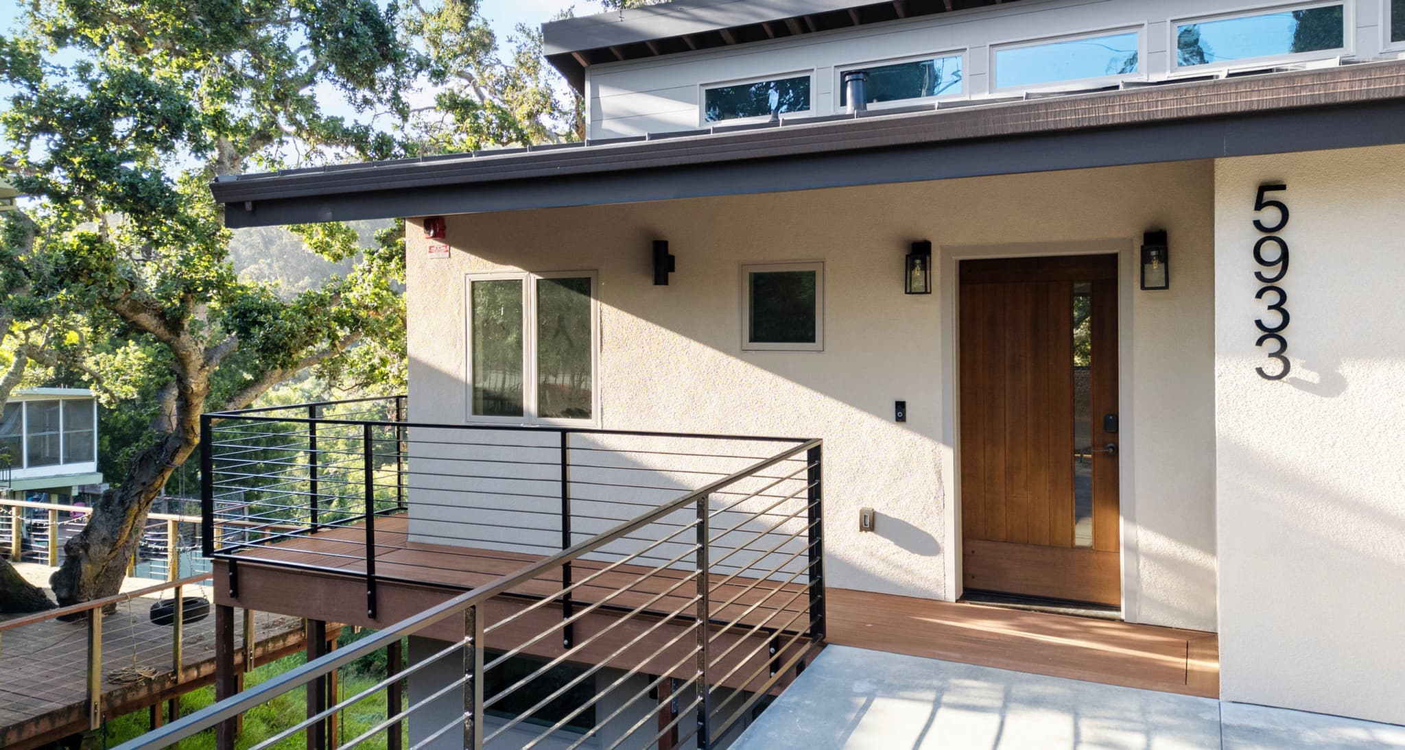 Modern two-story home exterior with clerestory windows, deck, and cable railing on a wooded hillside